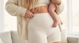 Mother holding baby while wearing high-waisted postpartum shaping shorts, illustrating when to start faja compression after a C-section