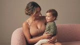 Mother wearing a front-closing post-surgical bra with no underwire while holding her toddler on a sofa